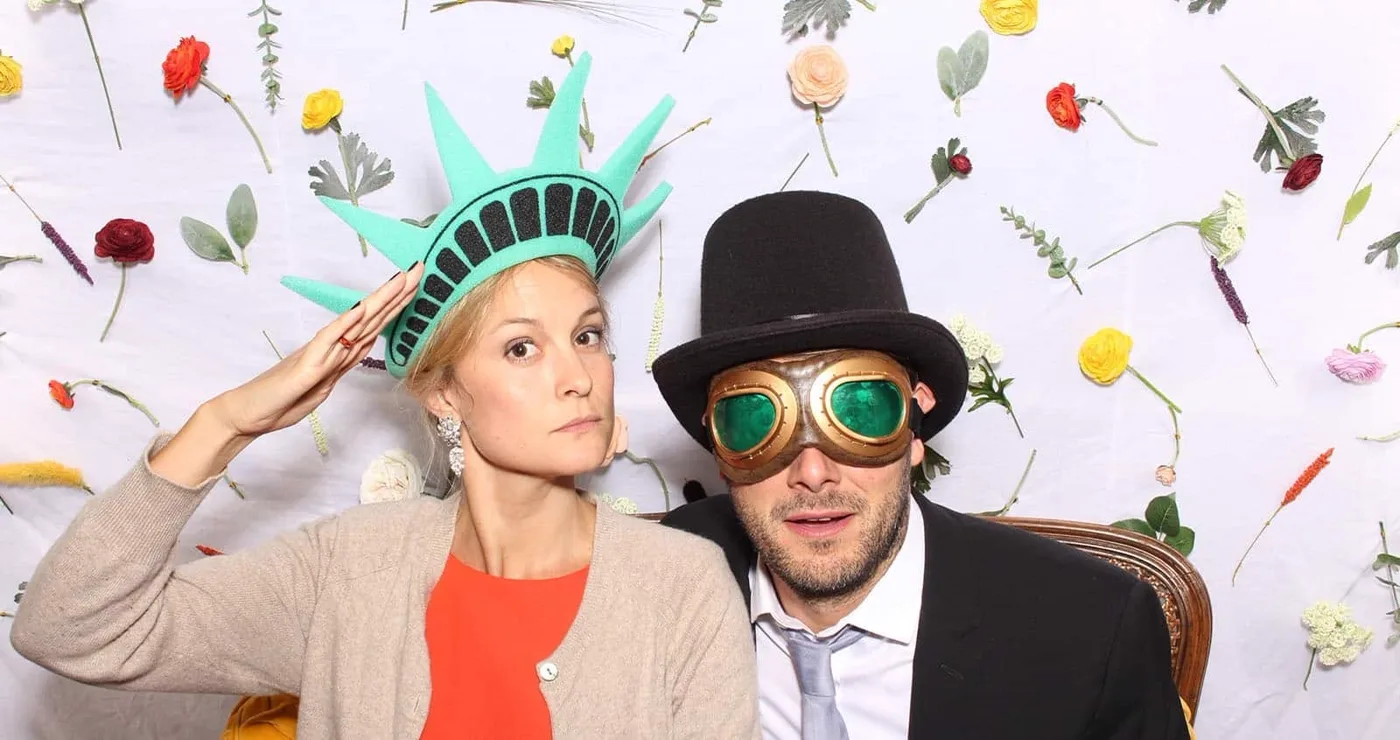Couple costumé, couronne de la statue de la Liberté et chapeau haut-de-forme, devant un mur fleuri